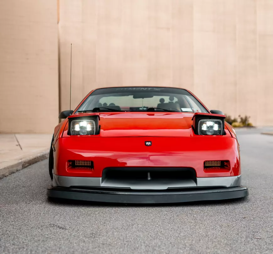 The front of a 1986 Pontiac Fiero GT shot by stance auto magazine photographers with its lights popped up